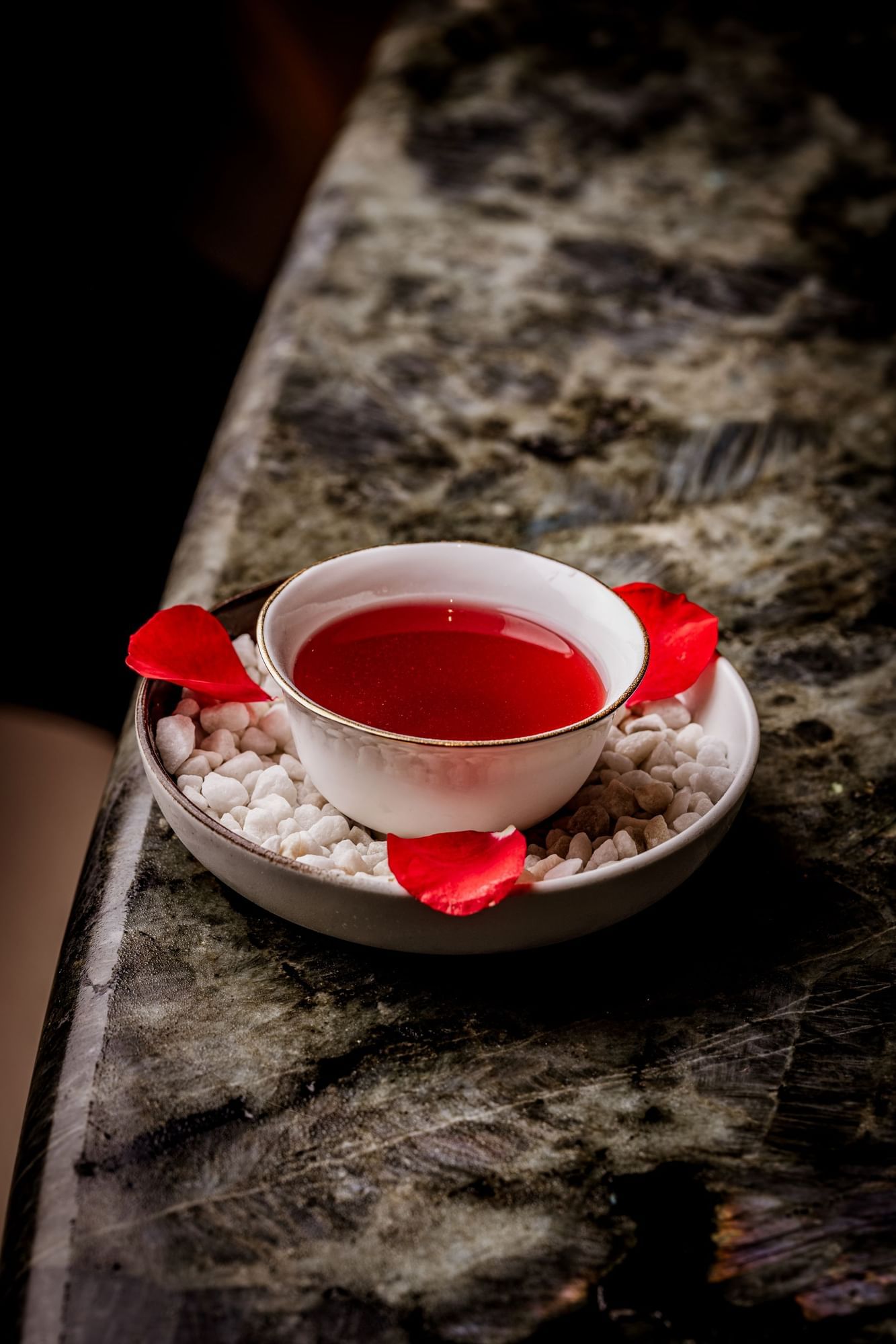 White bowl with a red cocktail inspired by Morocco Rosa and rose petals on a marble surface at The May Fair Bar