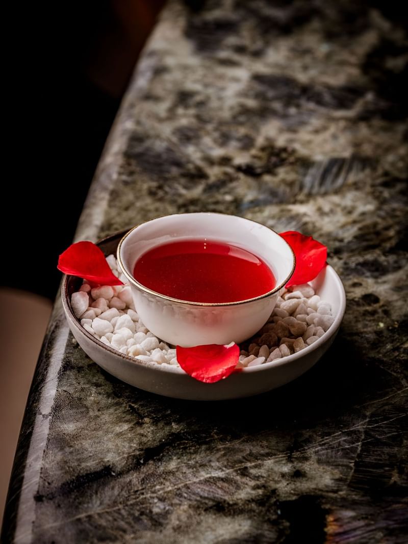 White bowl with a red cocktail inspired by Morocco Rosa and rose petals on a marble surface at The May Fair Bar