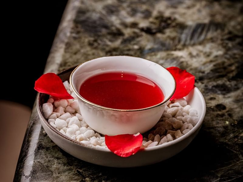 White bowl with a red cocktail inspired by Morocco Rosa and rose petals on a marble surface at The May Fair Bar