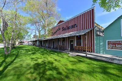 Building with red and white stripes and a long porch beside a green lawn at Buffalo Bill Village