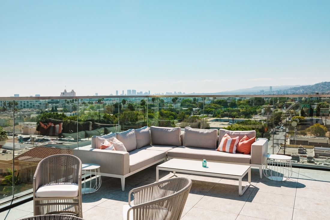 A rooftop patio with a city skyline view, featuring a sectional sofa, coffee table, and chairs.
