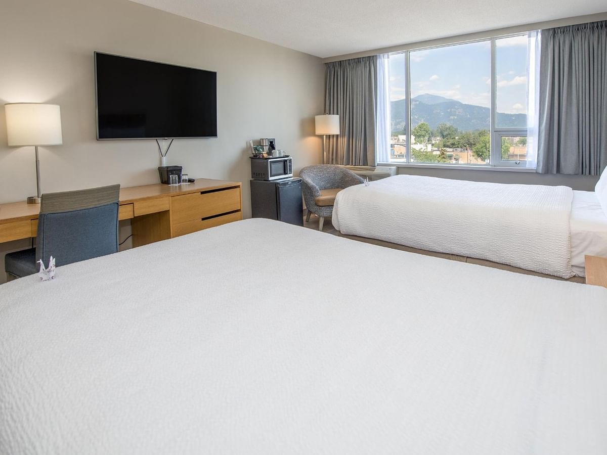 Two queen beds with work desk, TV, fridge, and microwave in a hotel room.