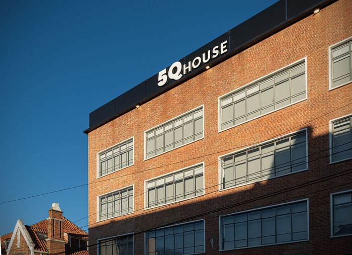 Red brick exterior of 5Q House Quinta Camacho with tall modern windows and bold logo on black top under clear blue sky