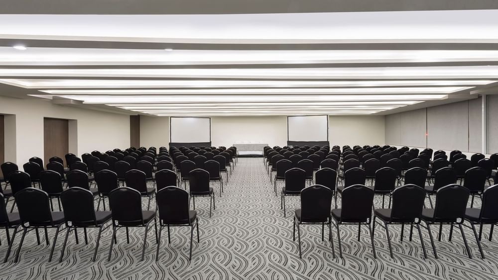 Large conference hall with theater-style seating and dual projection screens for events at Real Inn Celaya