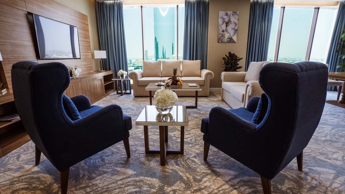 Two navy wingback chairs by a glass table facing a beige sofa in Ambassador Suite at Cantonal Hotel by Warwick Riyadh