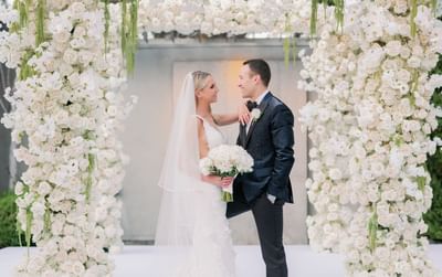 A wedding couple posing by a floral arch in a ballroom at Luxe Sunset Boulevard Hotel