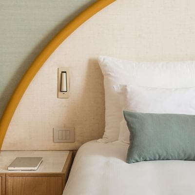 A hotel bed with headboard, white and green pillows, and a yellow lamp on the nightstand.