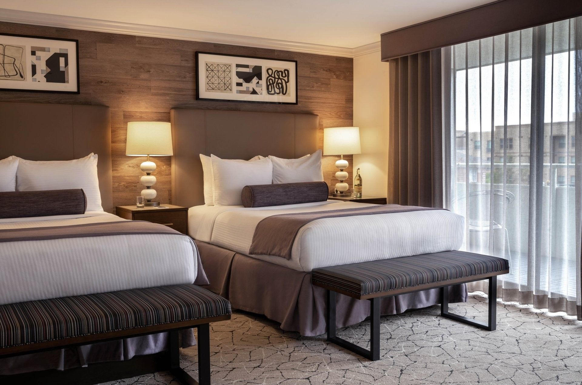 Two beds by striped benches under warm lamps and wood-style wall panels in Classic Double Room at Warwick Denver