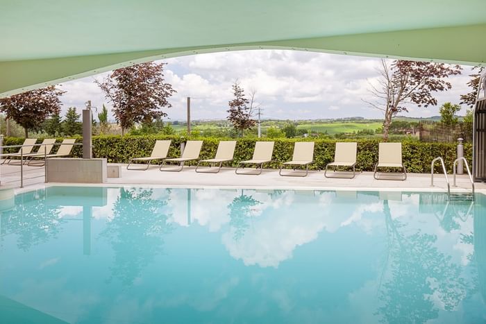 Outdoor pool with lounge chairs and greenery, under a curved green canopy with a scenic view.