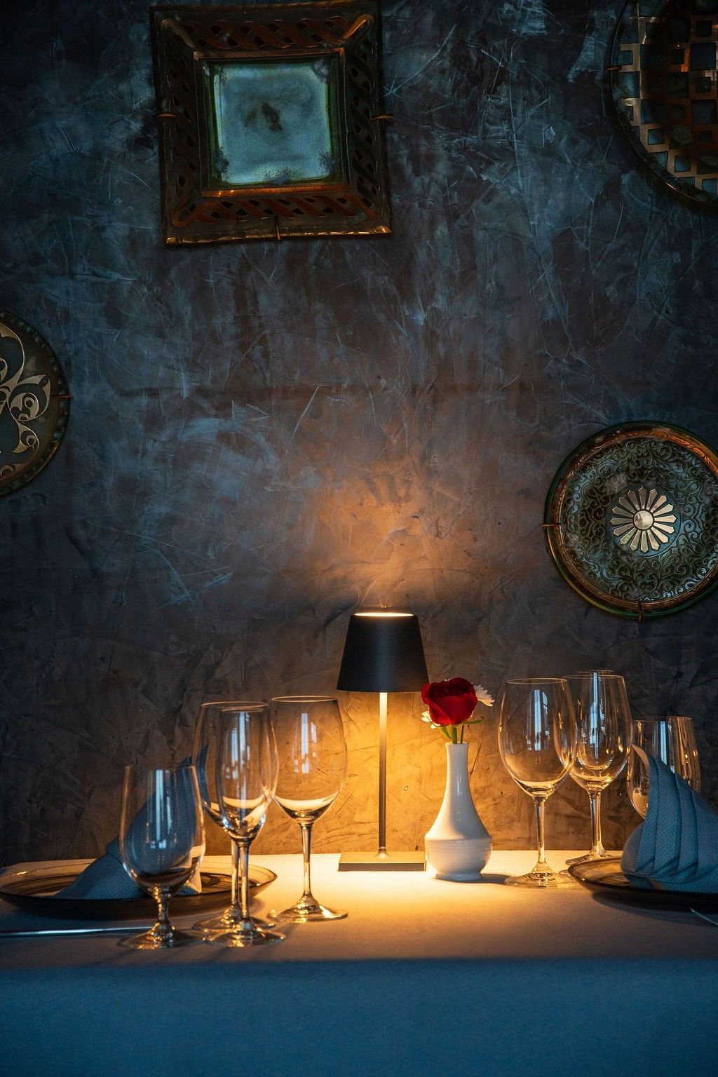 Intimate dining table with wine glasses, lamp, and red rose against textured blue wall at Marquis Los Cabos Resort & Spa