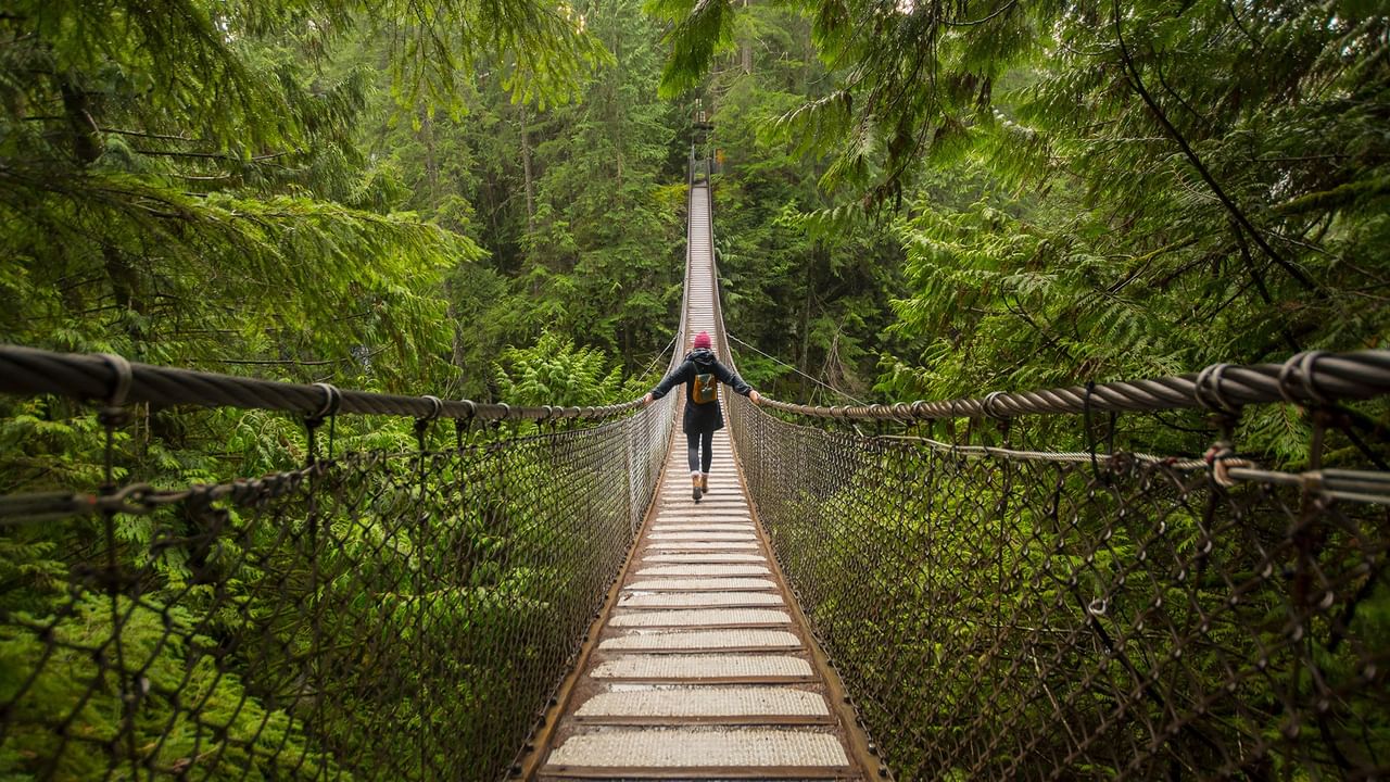 A person wearing a pink hat walks on a suspension bridge surrounded by lush forest near Coast Lonsdale Quay Hotel 
