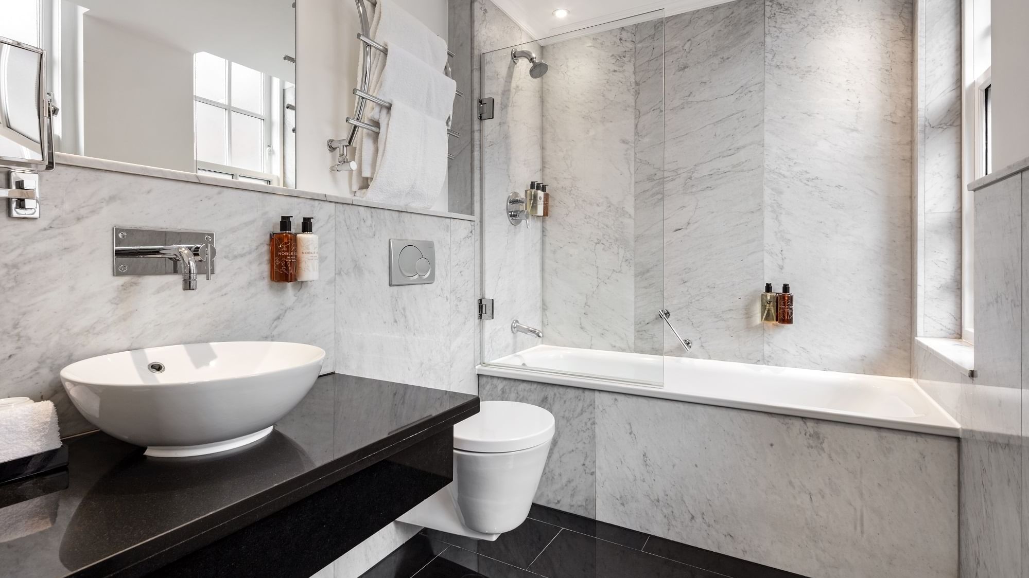Sleek bathroom in the Collection Deluxe Room at The May Fair Hotel with sink on black countertop, toilet, and bathtub