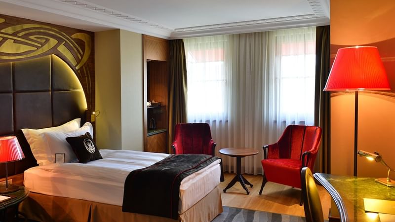 Bed, red comfy chairs, and working desk in Deluxe Twin Room at Warwick Ankara