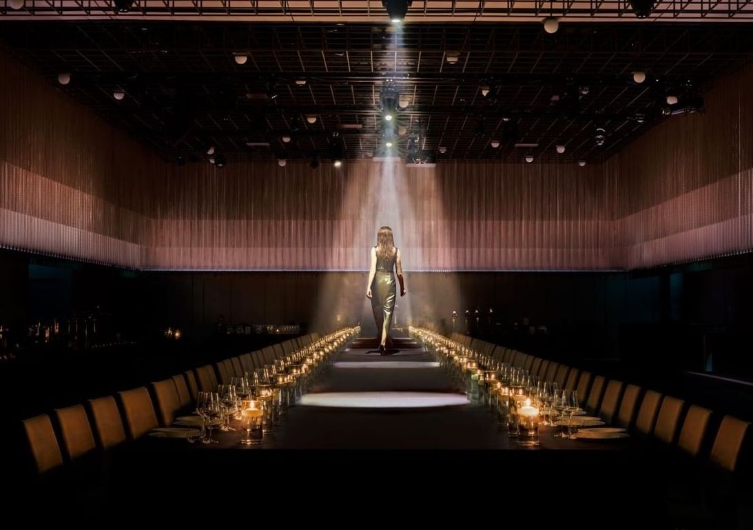 Uma imagem impressionante de uma mulher a caminhar ao longo de uma longa mesa iluminada por velas num deslumbrante espaço para eventos no The Londoner Hotel