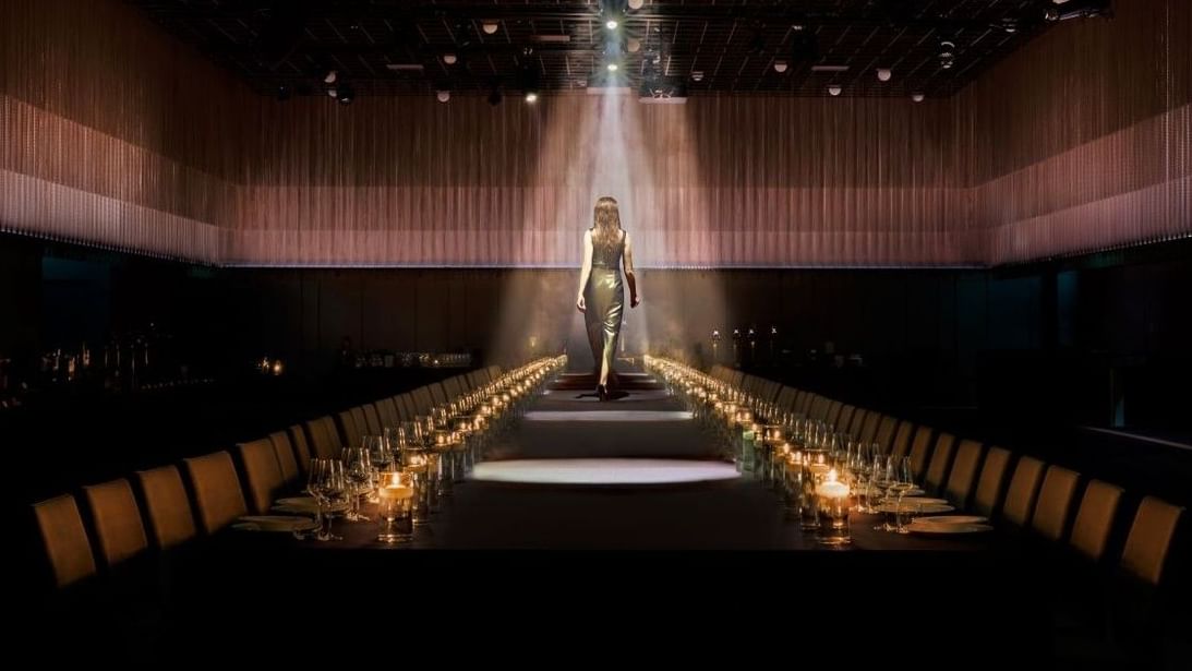 A dramatic shot of a woman walking down a long, candlelit table in a stunning event space at The Londoner Hotel