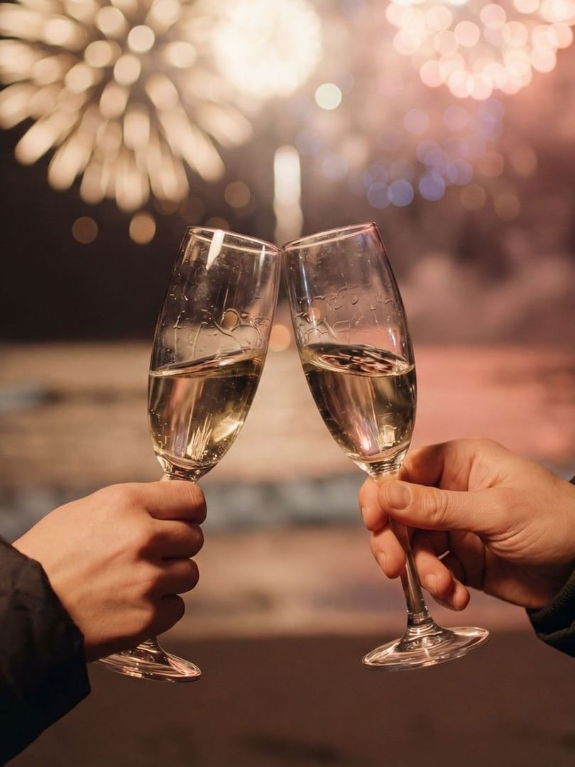 Deux personnes trinquent avec des flûtes de champagne devant un feu d'artifice illuminant le ciel nocturne
