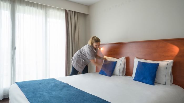 A lady arranging a bed in a room at Hotel Admiral's