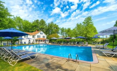 Relaxing pool area with blue loungers and umbrellas surrounded by greenery at Avon Old Farms Hotel