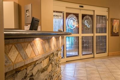 Front desk featuring a stone veneer with logo-adorned doors opening to the exterior courtyard at Hilltop Inn Salmon Arm