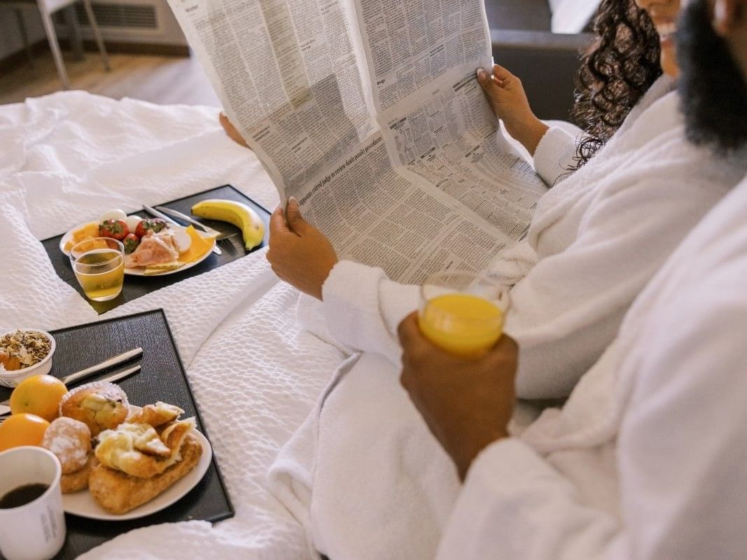 Couple in robes by breakfast trays at Paradox Bangkok Sukhumvit, reading a newspaper and enjoying a hotel offer in Bangkok