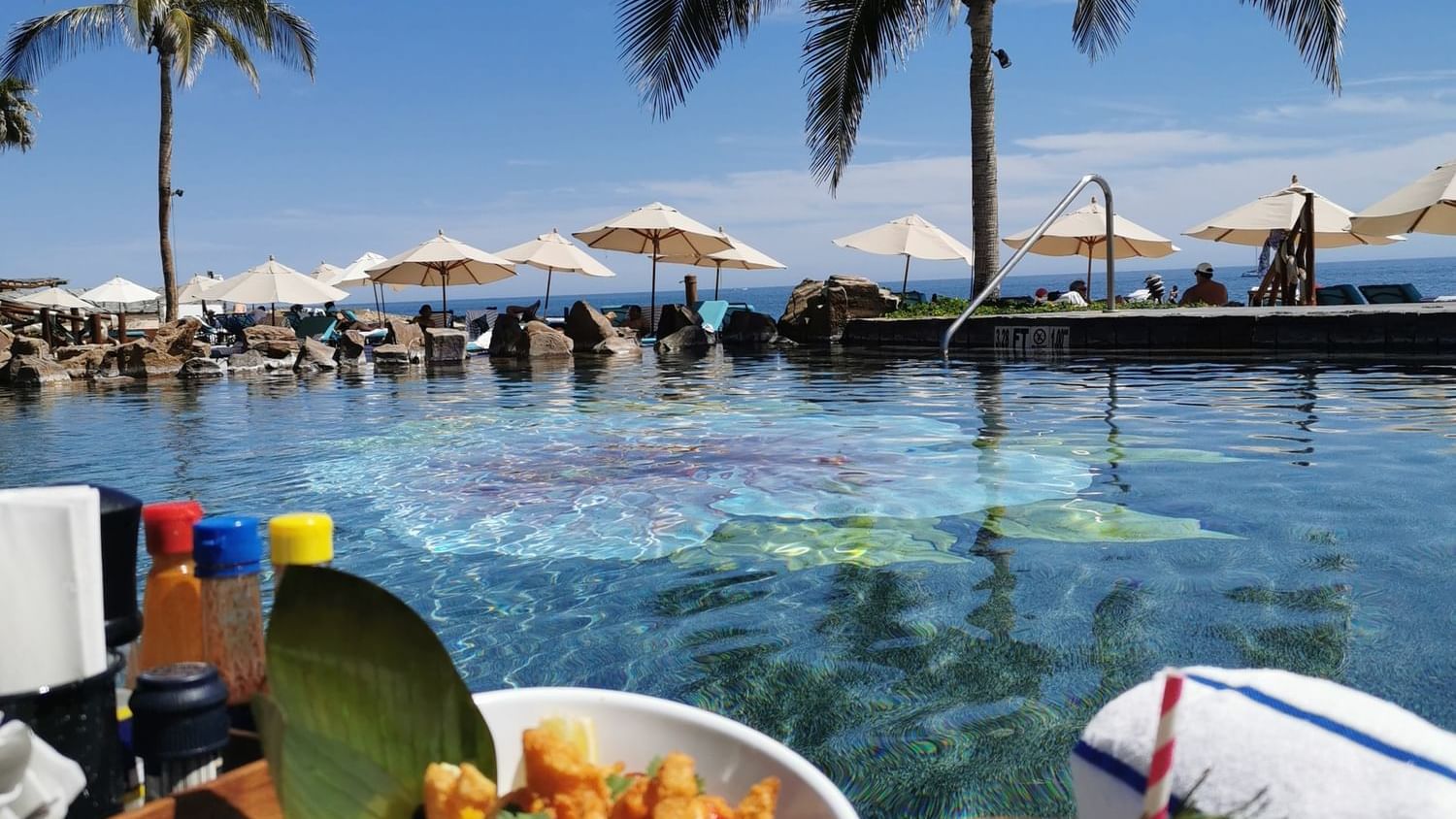Bowl of fried food and a cocktail on a table next to the pool and ocean at Sirenas Restaurant in Hacienda Del Mar Los Cabos.