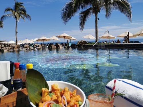 Bowl of fried food and a cocktail on a table next to the pool and ocean at Sirenas Restaurant in Hacienda Del Mar Los Cabos