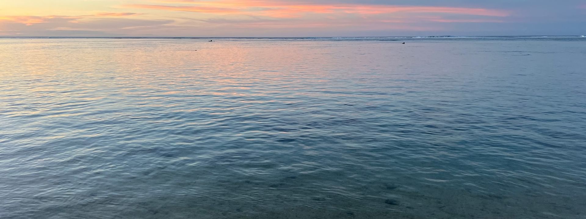 Calm ocean water by a sandy shore under a colorful sunset sky near Tambua Sands Beach Resort in Sigatoka.