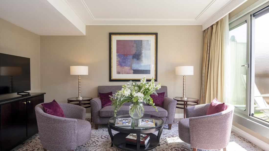 Purple sofa & armchairs surrounding a glass table under abstract art in The Montaigne Suite at Warwick Paris Champs Elysées