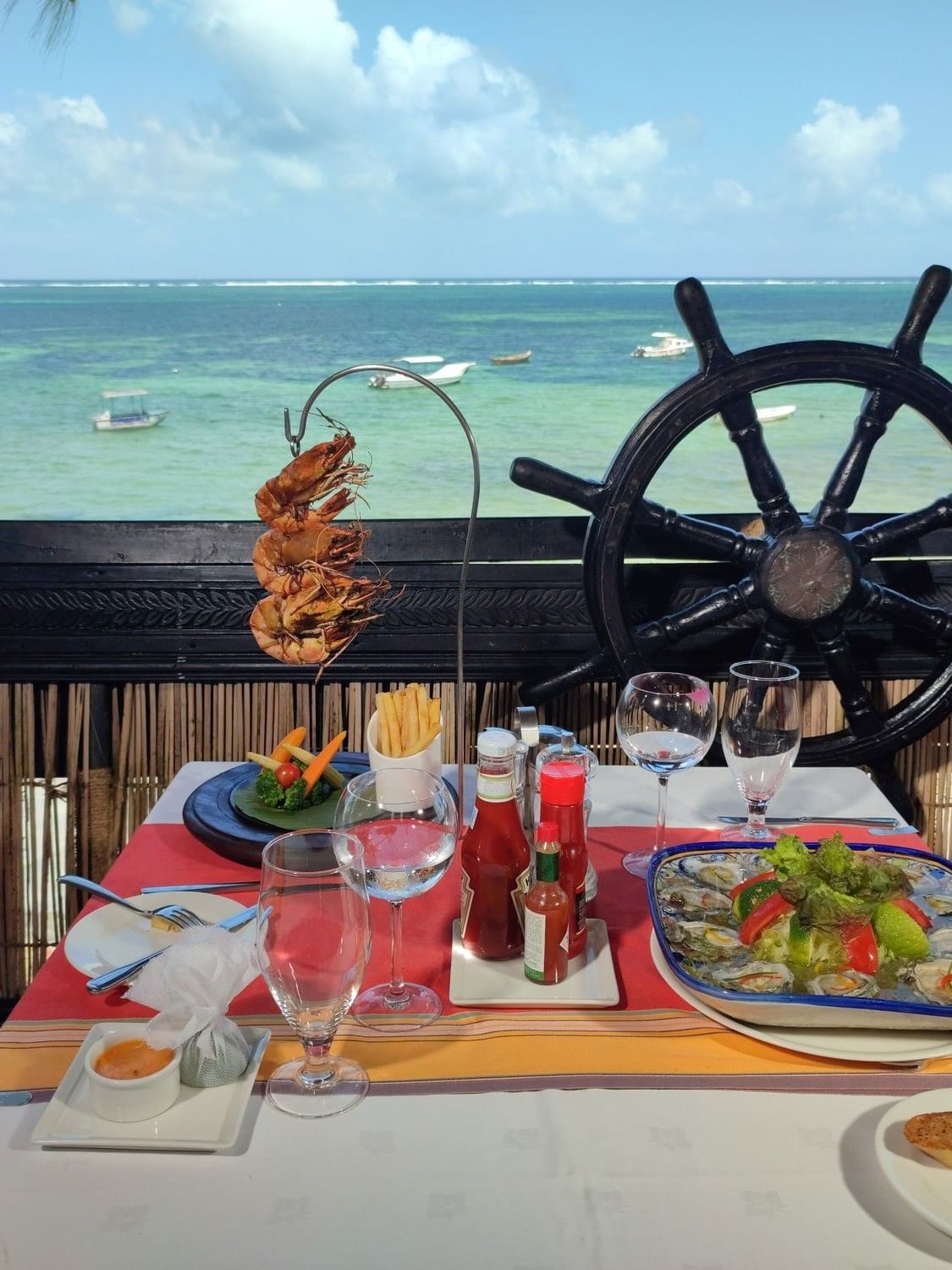 A coastal dining table with sea view and ship wheel decor at The Jahazi Grill, Serena Beach Resort & Spa in Mombasa.