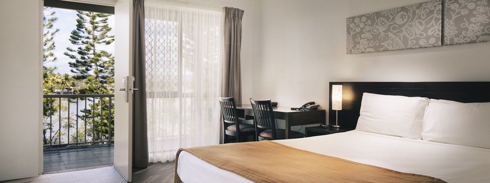 Standard room featuring a queen bed, a desk, and a balcony with a view of trees at Mercure Hotel Townsville