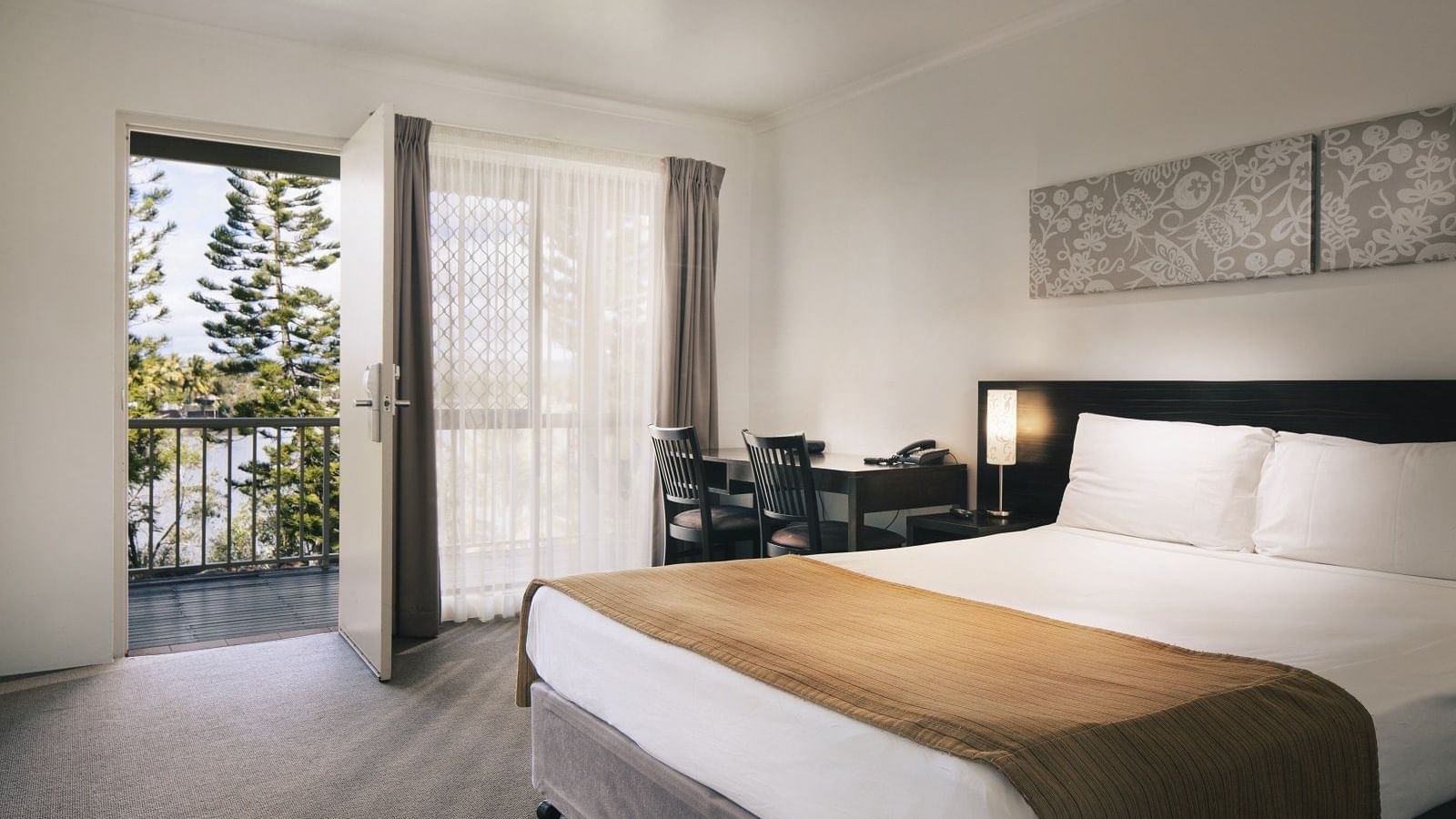 Standard room featuring a queen bed, a desk, and a balcony with a view of trees at Mercure Hotel Townsville