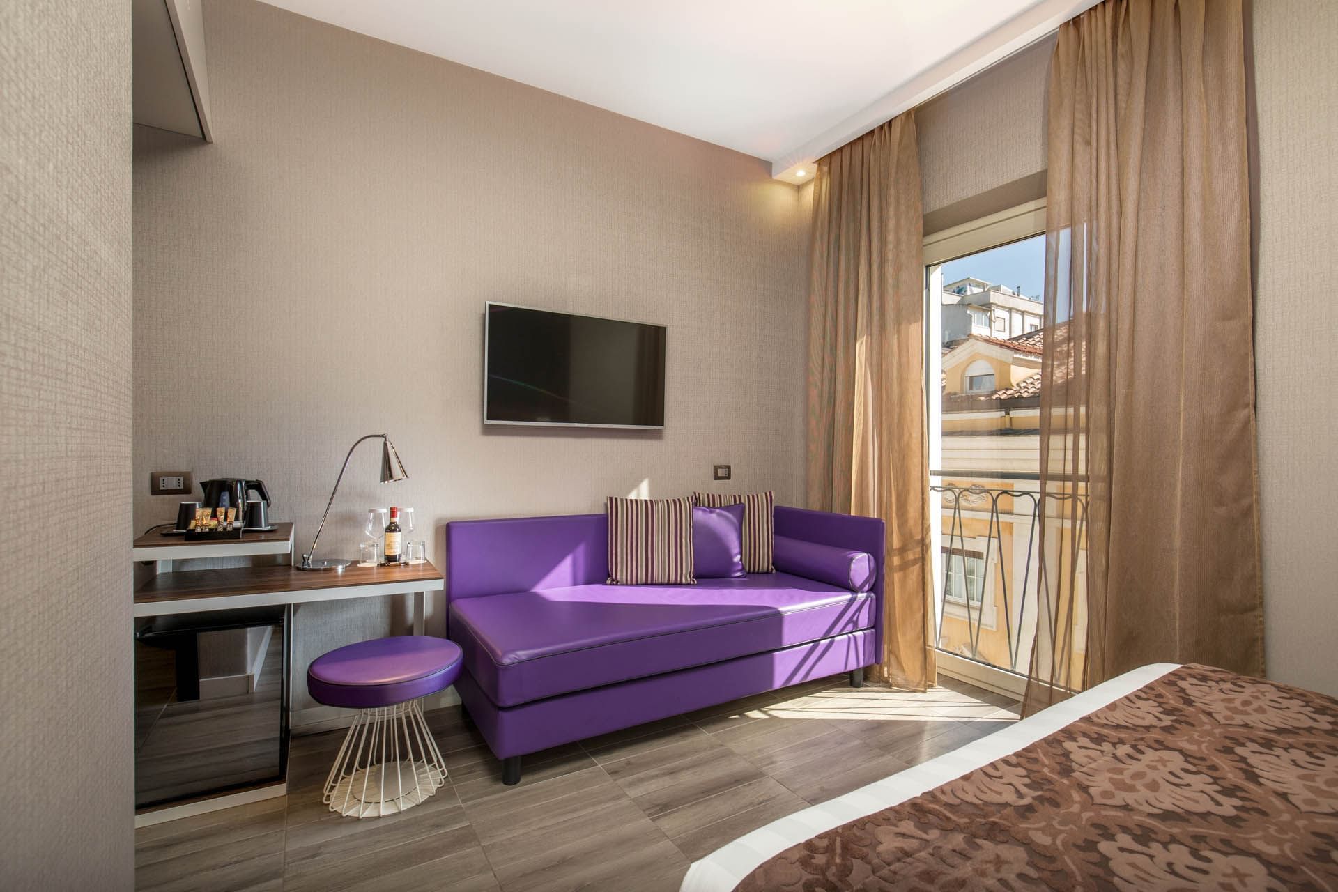 Cozy hotel room featuring a purple sofa, TV, coffee station, and large window with sheer curtains at The Republic Hotel