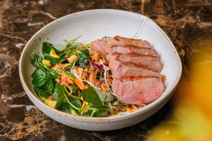 Salad bowl topped with thinly sliced, grilled beef, garnished with herbs, crunchy toppings, & veggies at Park Hyatt Saigon