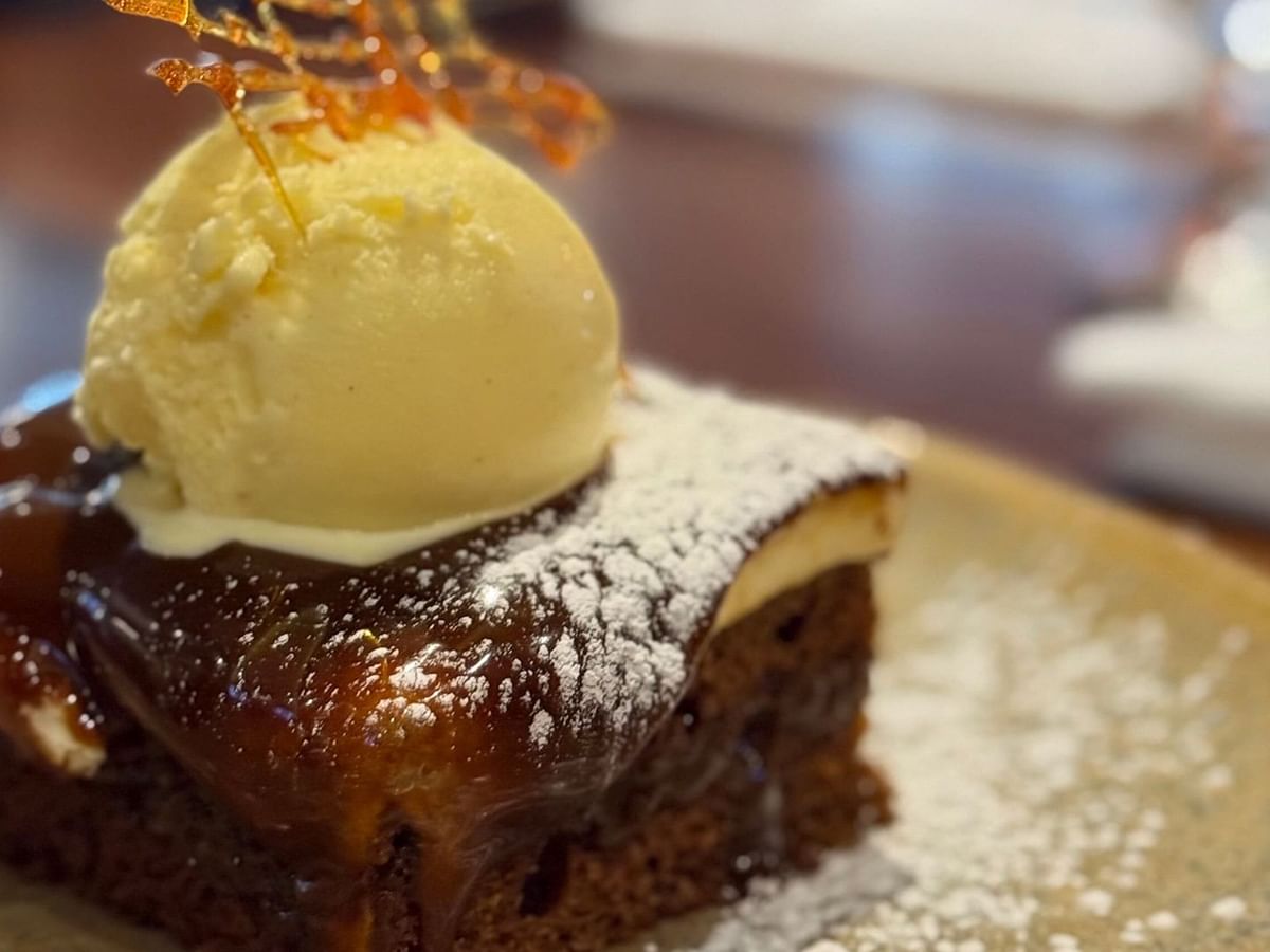 Carrot cake slice topped with ice cream and garnish, served on a plate with powdered sugar.