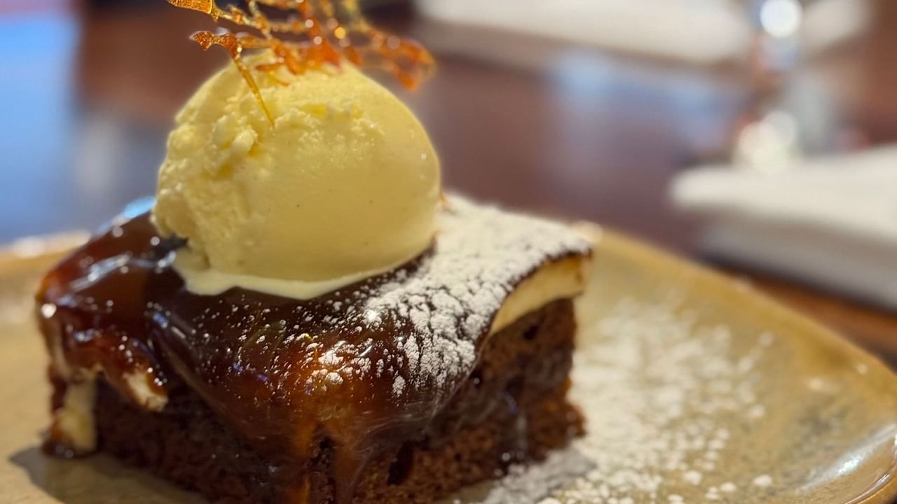 Carrot cake slice topped with ice cream and garnish, served on a plate with powdered sugar.