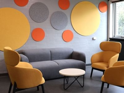 Lounge area with yellow and orange chairs, gray couch, and round table at La Trobe University Menzies College.