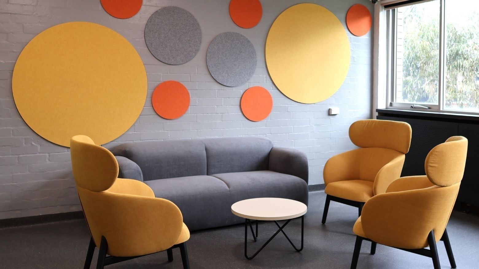 Lounge area with yellow and orange chairs, gray couch, and round table at La Trobe University Menzies College.