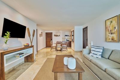 Bright and spacious living room with a sofa, coffee table, TV, and dining area in the background.