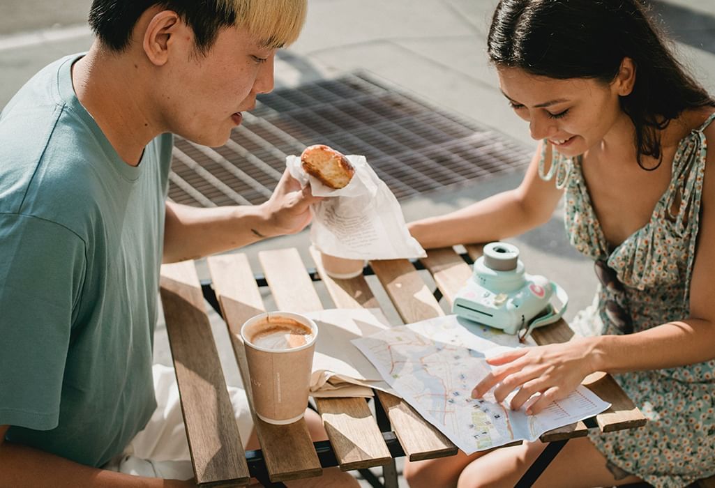 couple enjoys coffee and pastry while planning travel over a map