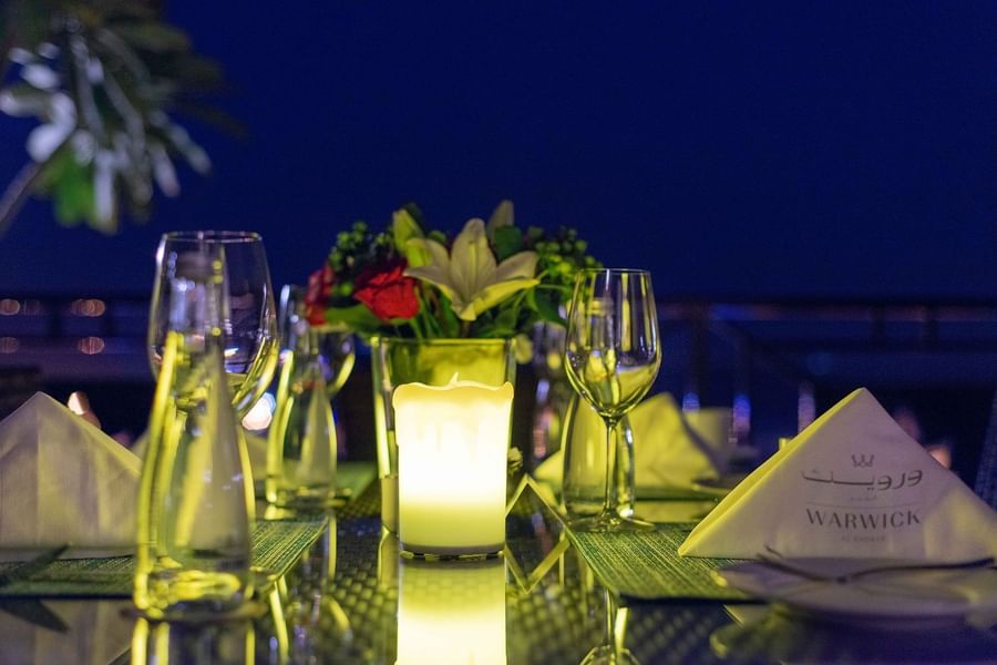 Soft yellow candlelight illuminating a set table with fresh floral centerpieces at Warwick Al Khobar