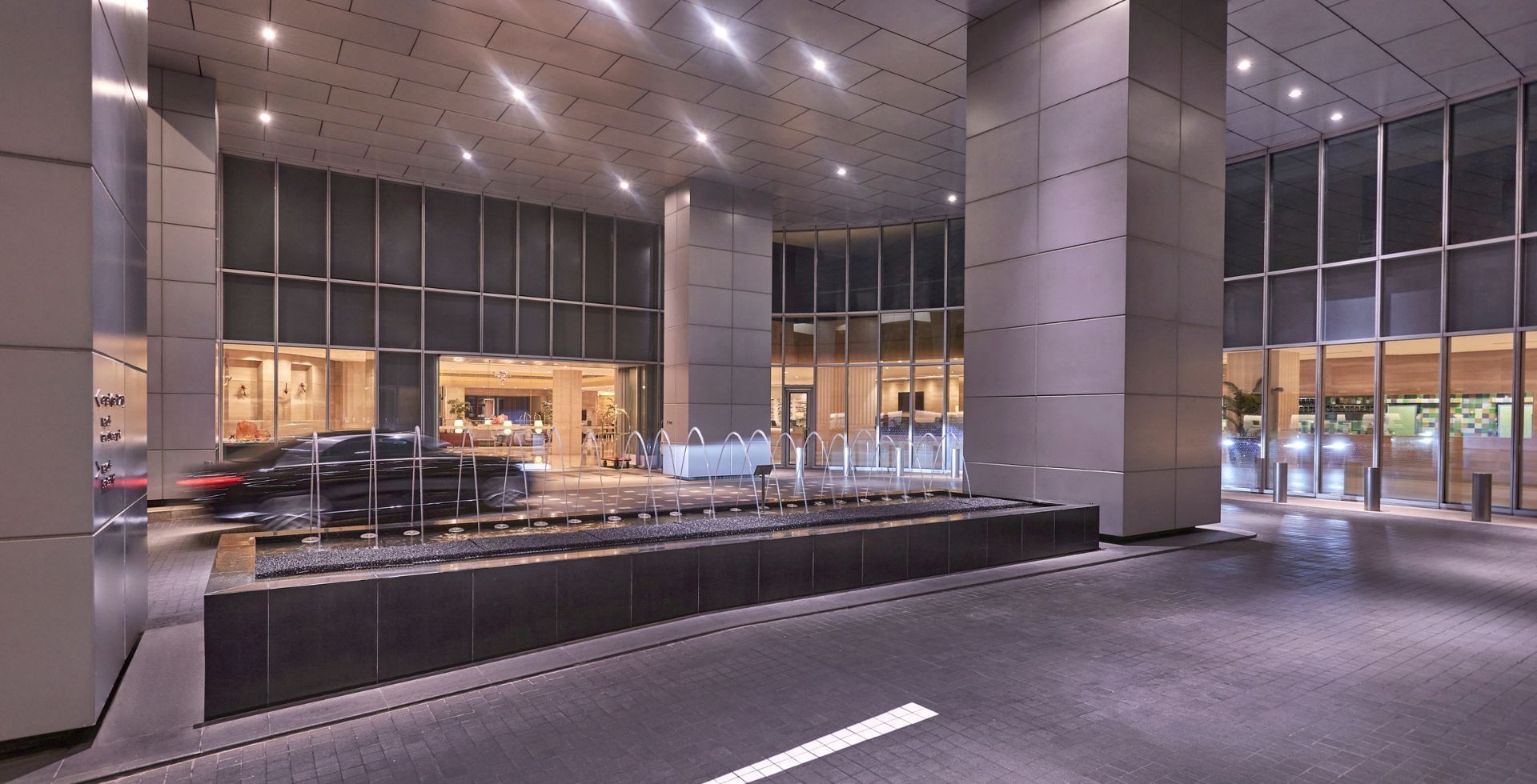 The brightly lit modern hotel entrance with a sleek fountain and a car arriving at Carlton Hotel Singapore