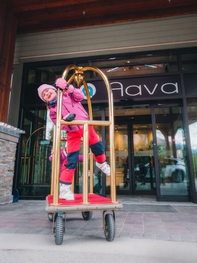A kid riding on a bellman's cart at Aava Whistler Hotel
