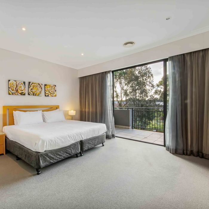 Two Bedroom Apartment with a large bed, art above a headboard, and sliding doors to a balcony at Mercure Kooindah Waters