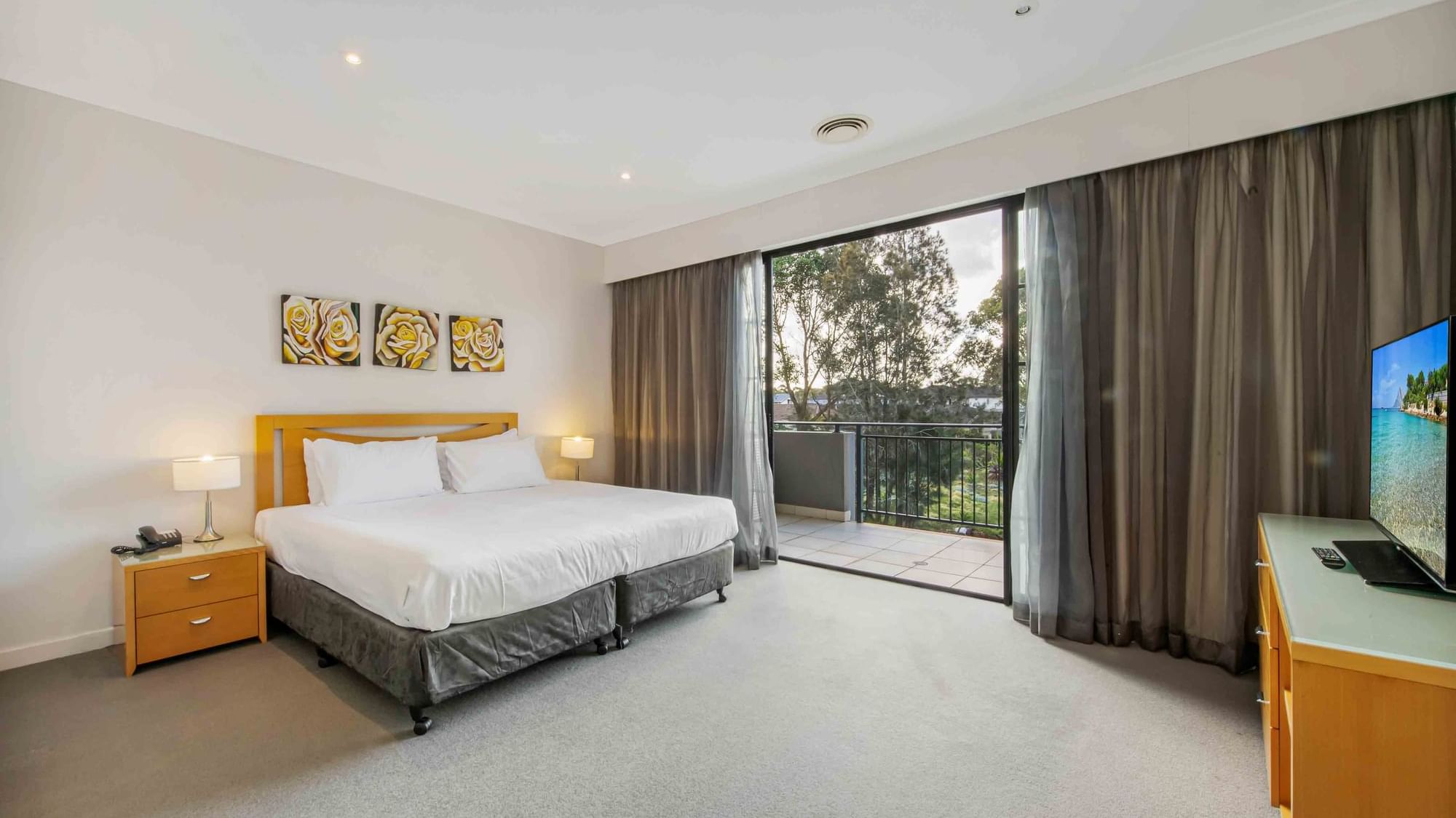 Two Bedroom Apartment with a large bed, art above a headboard, and sliding doors to a balcony at Mercure Kooindah Waters