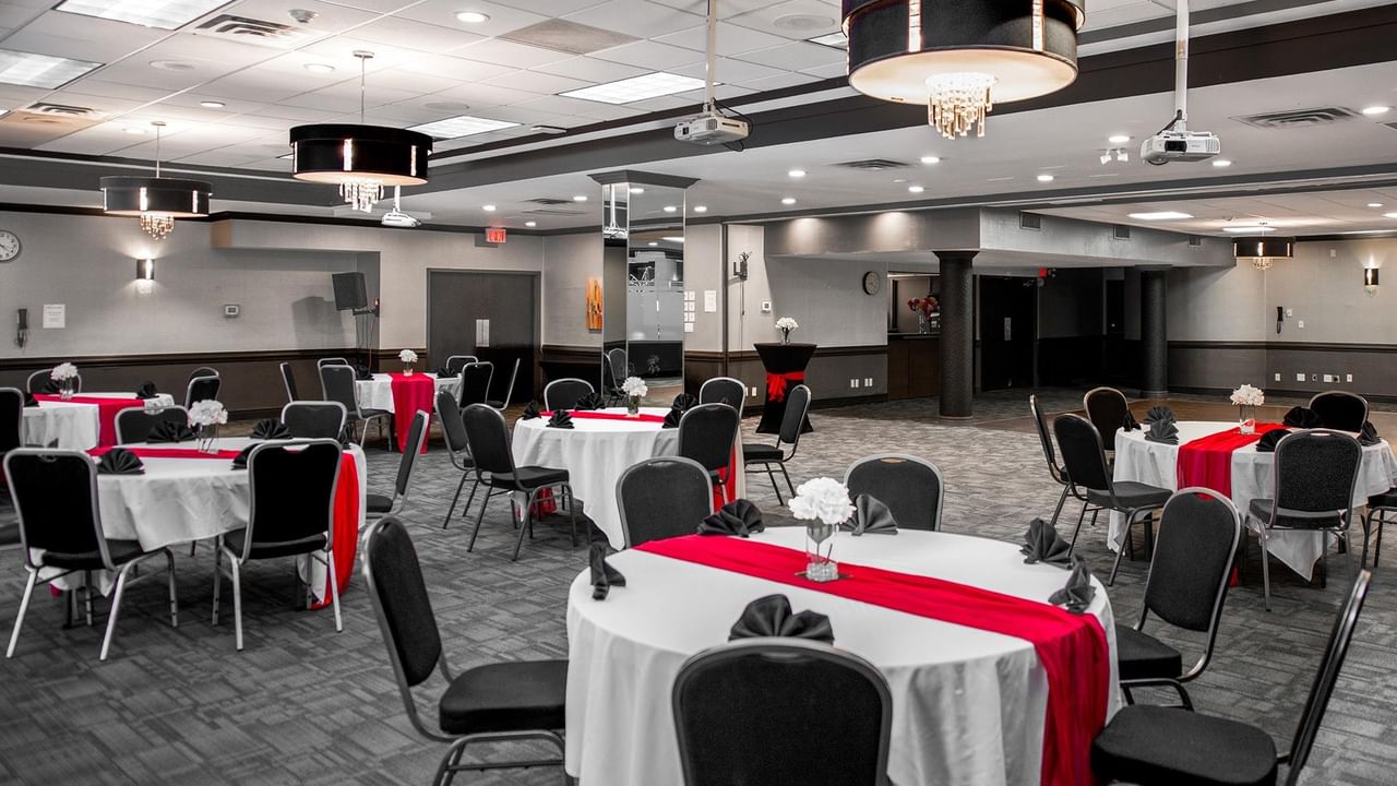 Spacious event room with round tables dressed in white linens and red runners at Coast Calgary University Area Hotel by APA