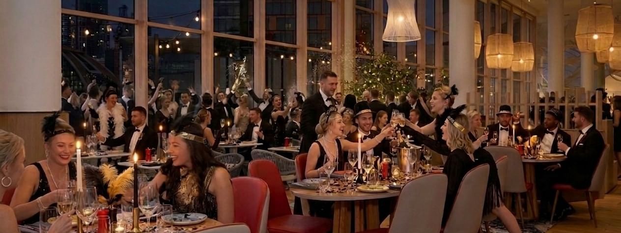 Two champagne flutes filled with sparkling wine, wrapped in gold ribbon and surrounded by festive bokeh lights, celebrating New Year's Eve at The Ternary, Darling Harbour.