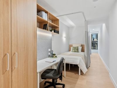 A compact modern room with a bed, desk, and wooden closet at UniLodge Brisbane City.