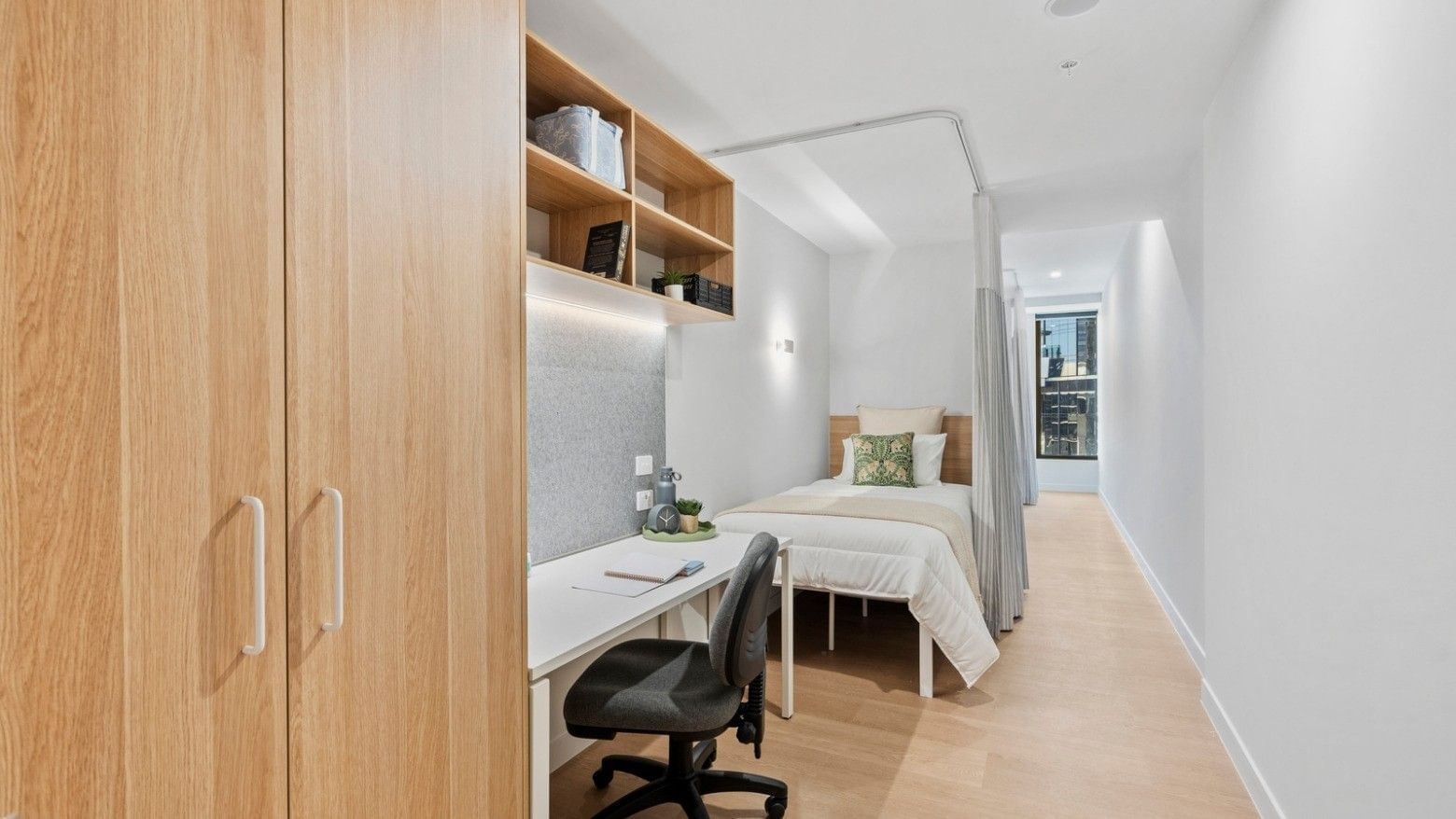 A compact modern room with a bed, desk, and wooden closet at UniLodge Brisbane City.