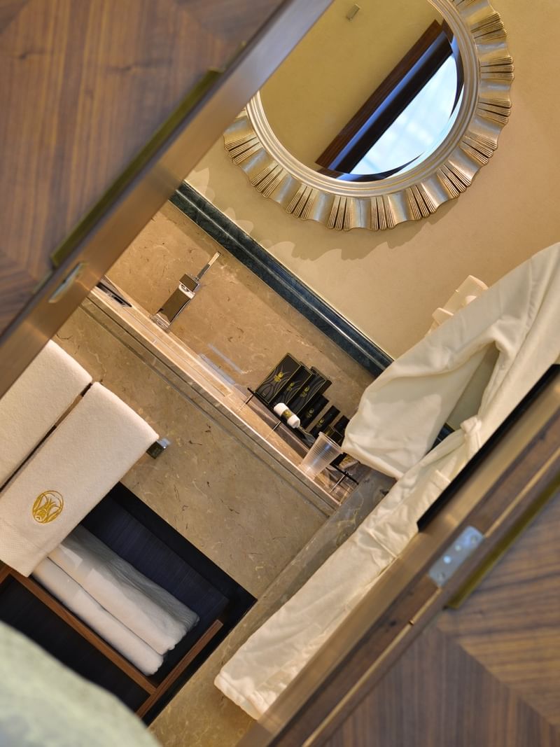Marble vanity by a sunburst mirror under warm light seen through a wooden door in Ankara Suite with Terrace at Warwick Ankara