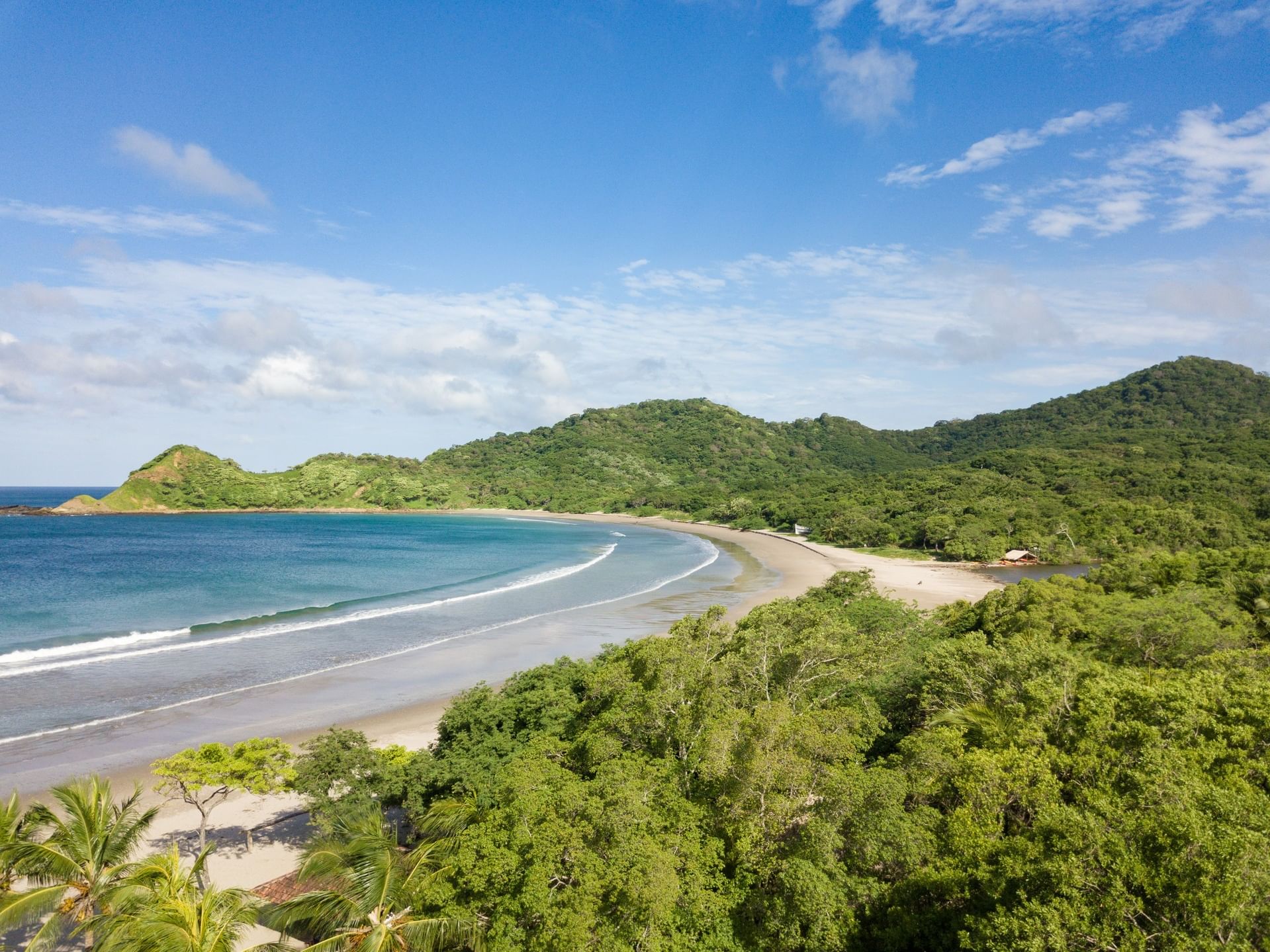 Curved sandy beach by a blue ocean under a bright sky and green hills near Morgan's Rock Reserve & Ecolodge